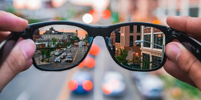 A pair of glasses, held up and reflecting a city street