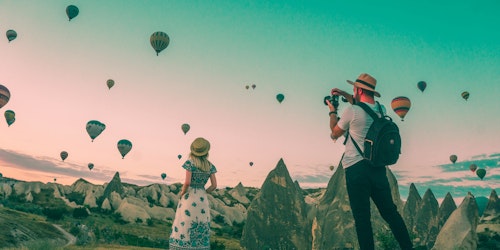 Two influencers, posing in front of a sky full of hot air balloons