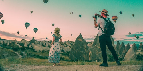 Two influencers, posing in front of a sky full of hot air balloons