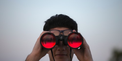A pair of binoculars facing the camera, with red lenses