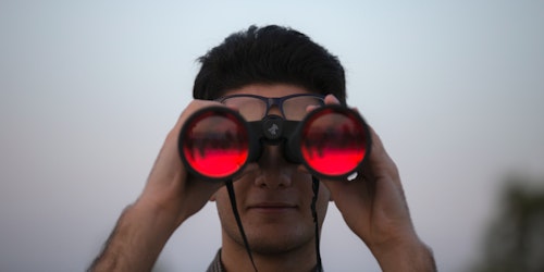 A pair of binoculars facing the camera, with red lenses