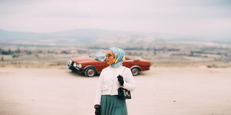 A stylishly dressed Muslim woman in front of a sports car