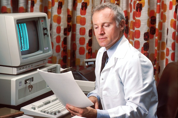 A man in a labcoat at a computer in front of a curtain