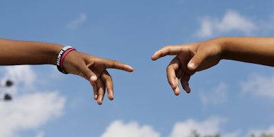 Two young people's hands reaching out, in an imitation of Michelangelo's The Creation of Adam