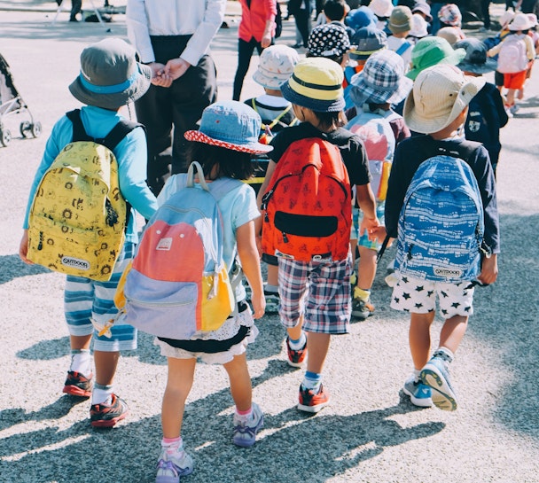 School children with giant backpacks crossing a road