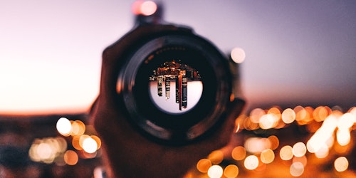 A city, reflected upside-down in a lens held by a hand