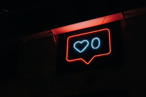 A neon sign of an Instagram-style heart icon, with zero likes