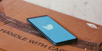 A phone showing the Twitter single on top of a cardboard box with the writing 'handle with care'