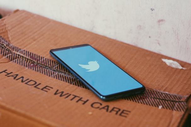 A phone showing the Twitter single on top of a cardboard box with the writing 'handle with care'