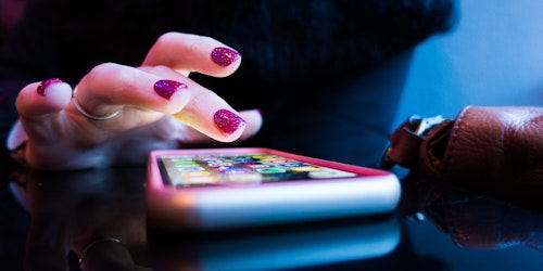 A person's hand hovering over a lit-up smart phone