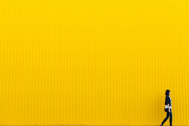 A woman walking in front of a yellow background