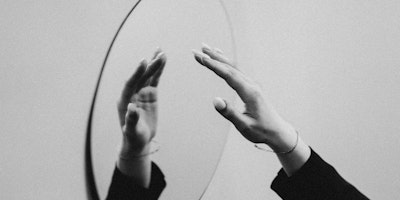 A hand reaching out to a mirror, in greyscale