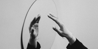 A hand reaching out to a mirror, in greyscale