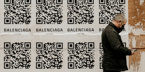 A man walking past a wall plastered with posters for Balenciaga, featuring QR codes