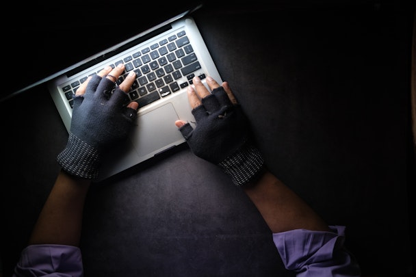 Hands in fingerless gloves typing on a laptop