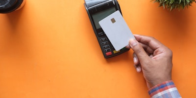 A hand holding a bank card, making a contactless payment