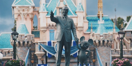 A statue of Walt Disney and Mickey Mouse, in front of a Disney pleasure resort