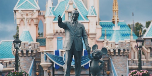 A statue of Walt Disney and Mickey Mouse, in front of a Disney pleasure resort