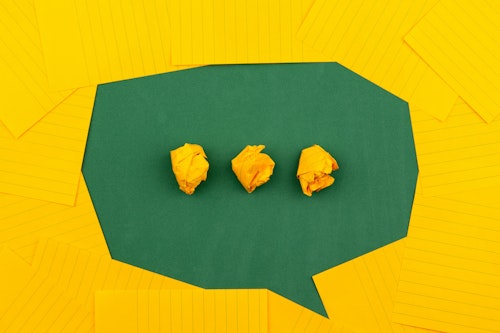 A green speech icon on a yellow background, made of paper
