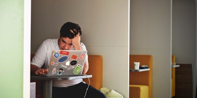 A marketer (man) has his head in his hands as he struggles to make Google Ads work on his laptop