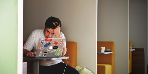 A marketer (man) has his head in his hands as he struggles to make Google Ads work on his laptop