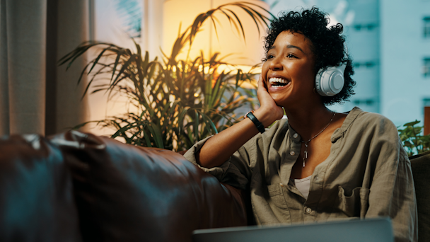 A woman listens to a brand's comedy podcast with headphones; she is laughing