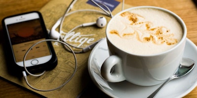 A phone with headphones playing a podcast influenced by AI technology, next to a cup of coffee