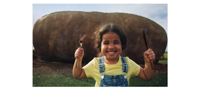child with silverware in front of a giant potato