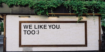 White brick wall with quote, "We like you, too :)" 