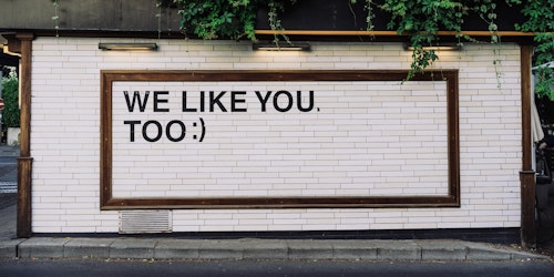 White brick wall with quote, "We like you, too :)" 