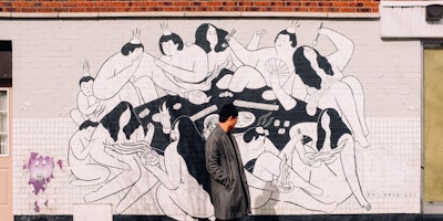 Man in black coat stood in front of mural
