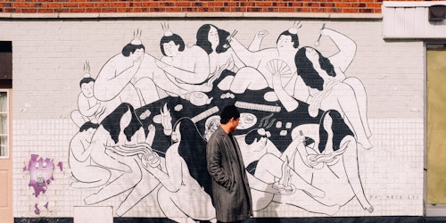 Man in black coat stood in front of mural
