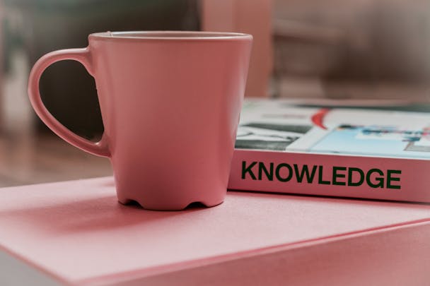 Book of knowledge next to a pink mug Book of knowledge next to a pink mug
