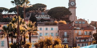 'Cannes' sign surrounded by palm trees and terracotta buildings 