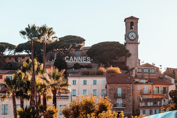 'Cannes' sign surrounded by palm trees and terracotta buildings 