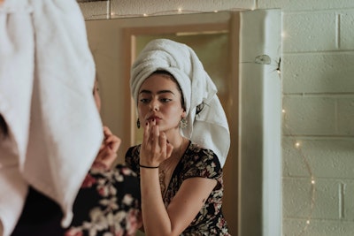 Gen Z woman applying makeup in mirror