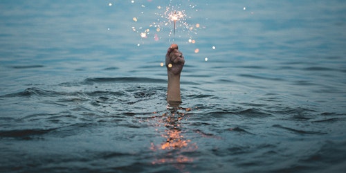 Person submerged in water holding up a sparkler