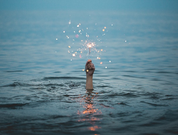 Person submerged in water holding up a sparkler