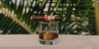 Cigar resting horizontally on top of a glass of whiskey