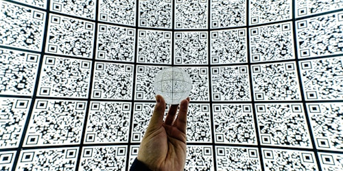 Person holding glass ball in front of wall of QR codes