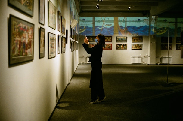Woman wearing face mask taking a photo at an art exhibiton