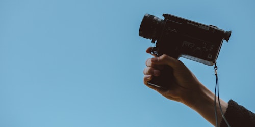Person holding video camera against blue background