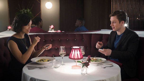A still from Netflix Black Mirror series showing a man and woman sitting across a table from one another