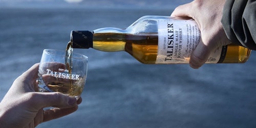 bottle of Talisker whisky being poured on a moody looking beach