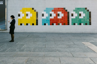 A person looking at their phone stands next to four differently coloured space invader characters of a wall