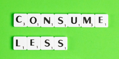 Scrabble letter pieces spell out the message 'consume less' against a green background