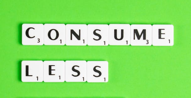 Scrabble letter pieces spell out the message 'consume less' against a green background Scrabble letter pieces spell out the message 'consume less' against a green background