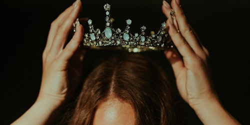 A person with long brown hair holds a crown over their own head