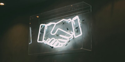 A white neon sign of hands holding against a concrete wall 