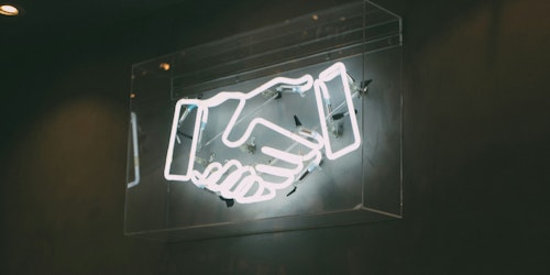 A white neon sign of hands holding against a concrete wall 